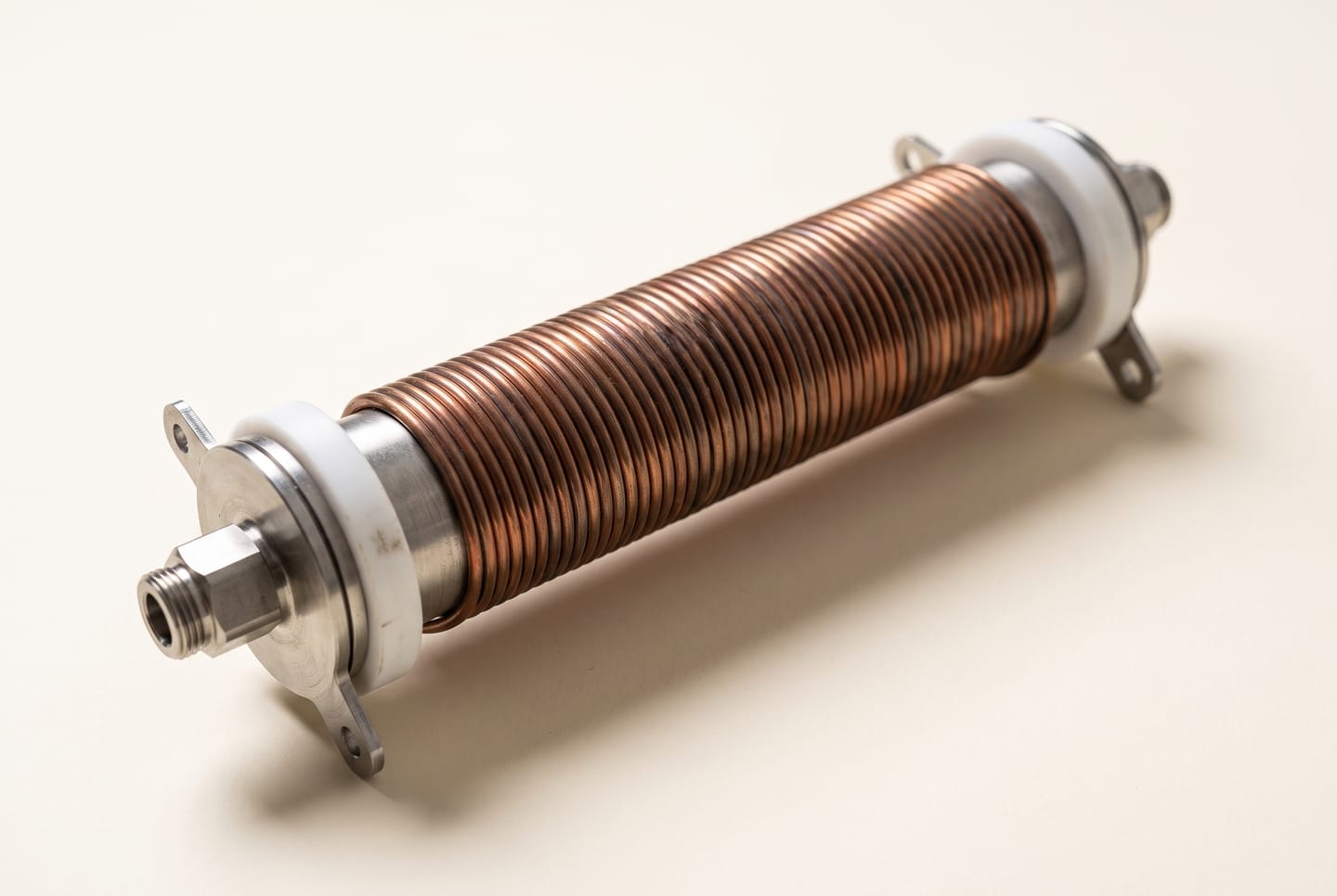Das Heylo Induktions-Heizelement: eine Kupferspule um ein Stahlrohr, mit weißen PTFE-Spulenkörpern und Stahlanschlüssen an beiden Enden