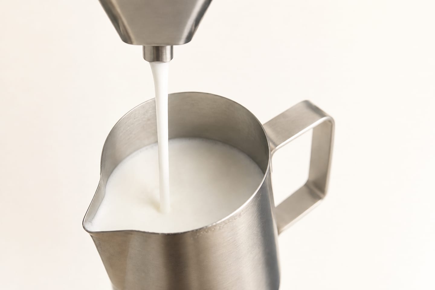 Texturierte Milch fließt aus einem einzelnen Stahlauslauf in ein Milchkännchen, ohne Dampf