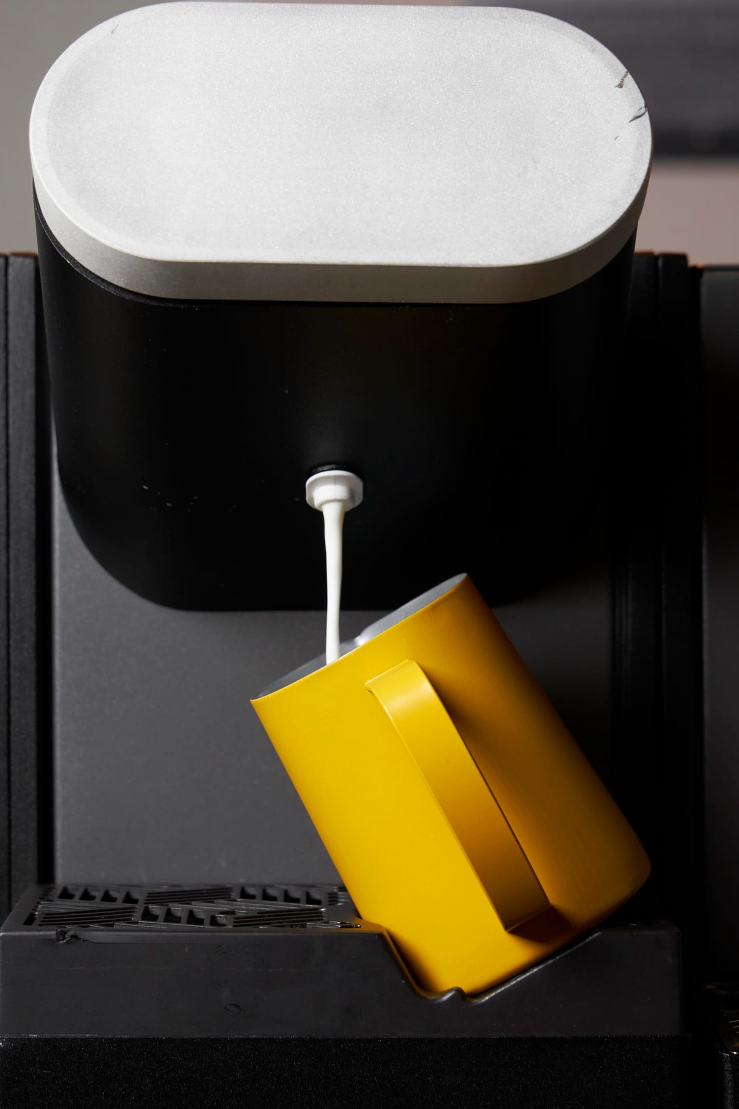 Testa di erogazione della Heylo Milk Unit che versa latte texturizzato in una lattiera gialla sul supporto lattiera inclinato